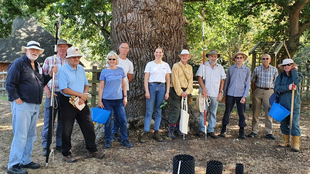 Eleven AONB volunteers stand in a line underneath a tree to pose outside for a photograph